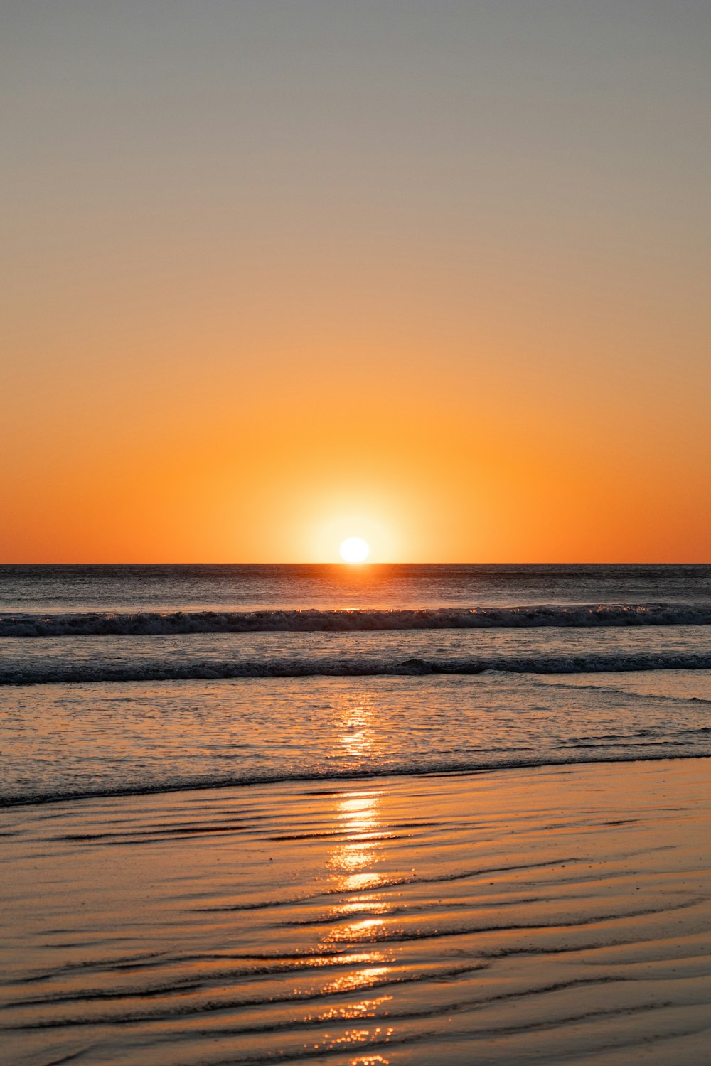 the sun is setting over the ocean on the beach