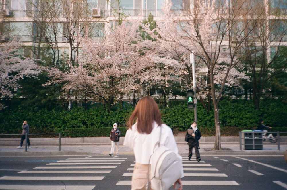 a woman walking across a cross walk in front of a building