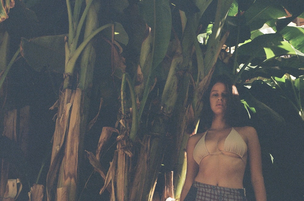 a woman in a bikini standing in front of a banana tree