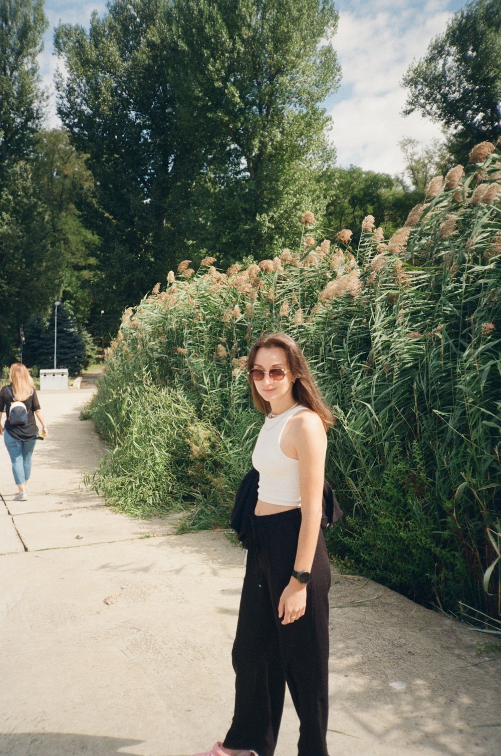 a woman standing on a sidewalk next to tall grass