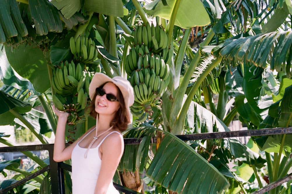 a woman wearing a hat and sunglasses standing in front of a bunch of bananas
