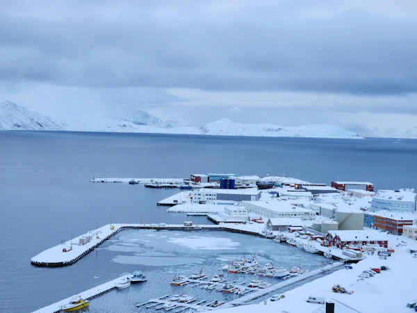 Snow-covered harbour and waterfront of Hammerfest with fishing boats and Arctic mountains across the sound