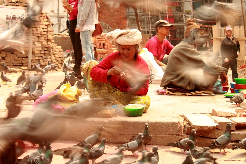 a woman sitting on the ground surrounded by pigeons