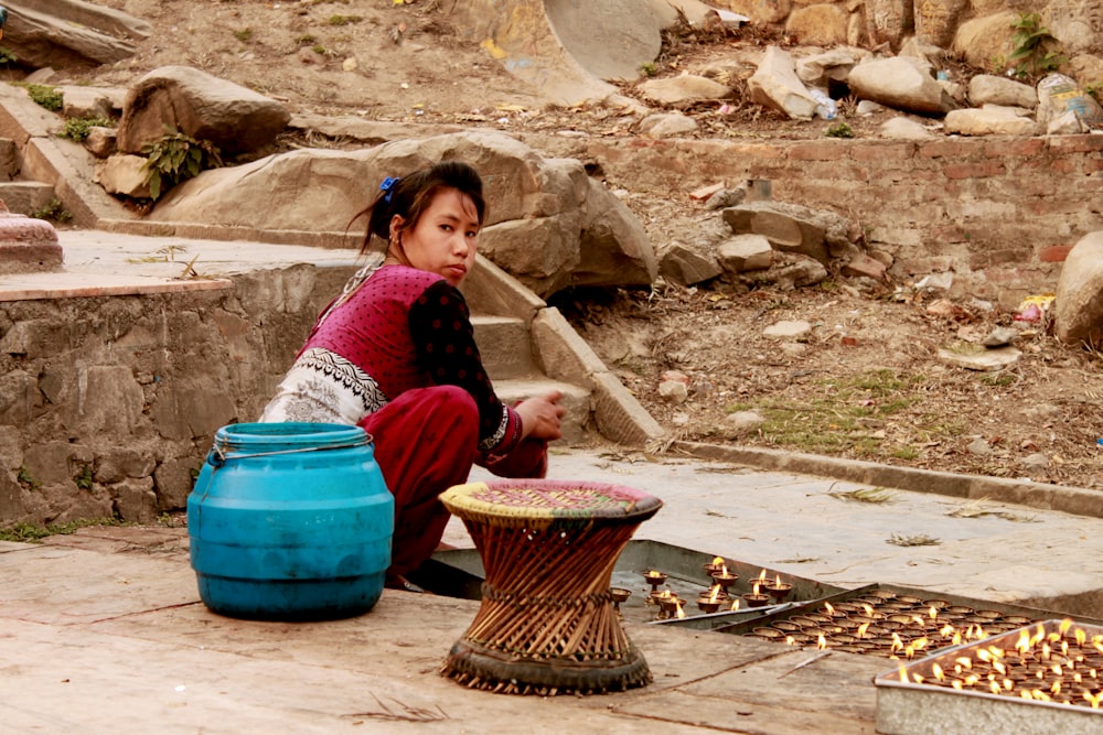 a young girl sitting on the ground next to a blue pot