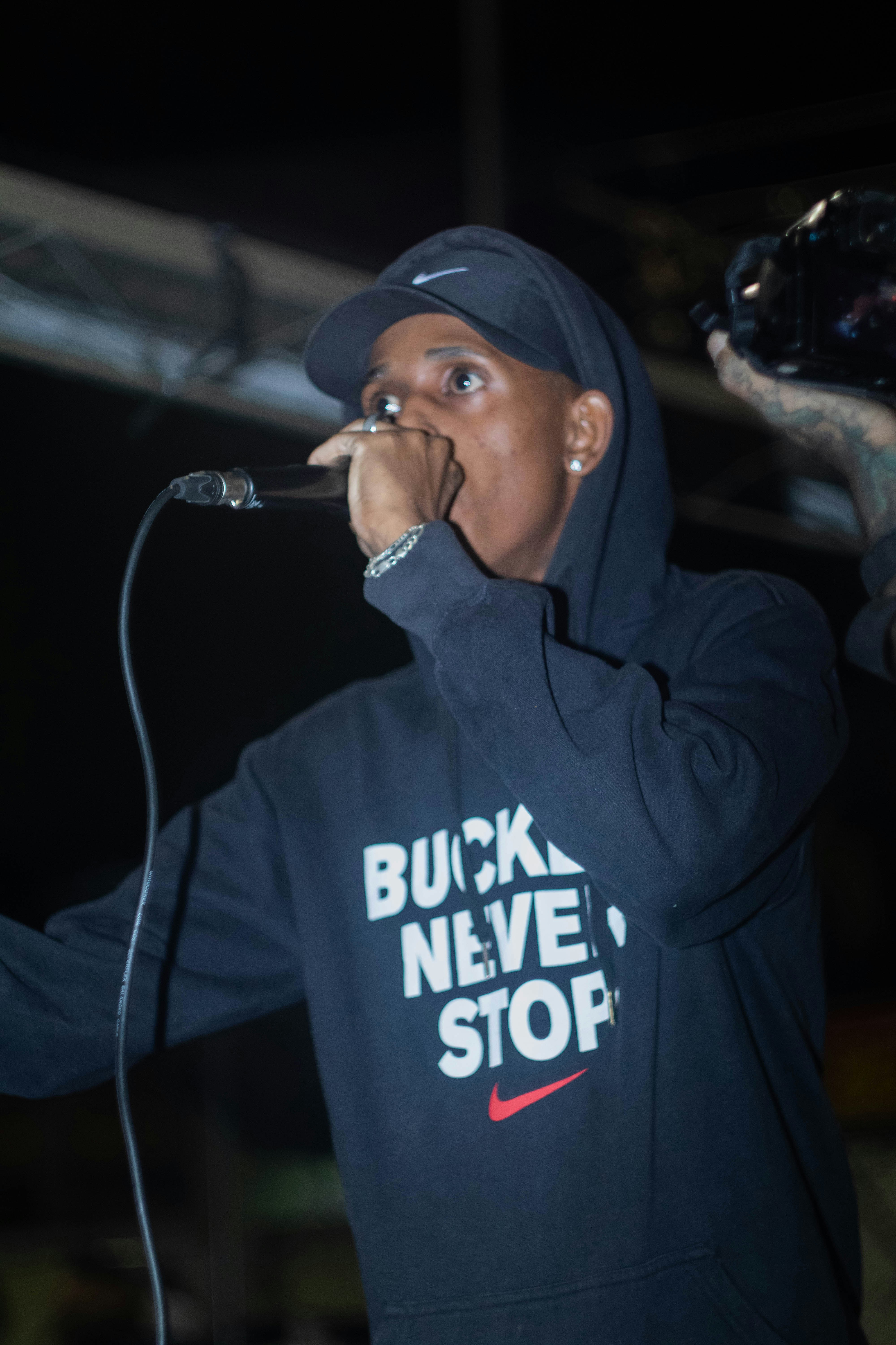 Seorang pria berhoodie hitam bernyanyi ke mikrofon