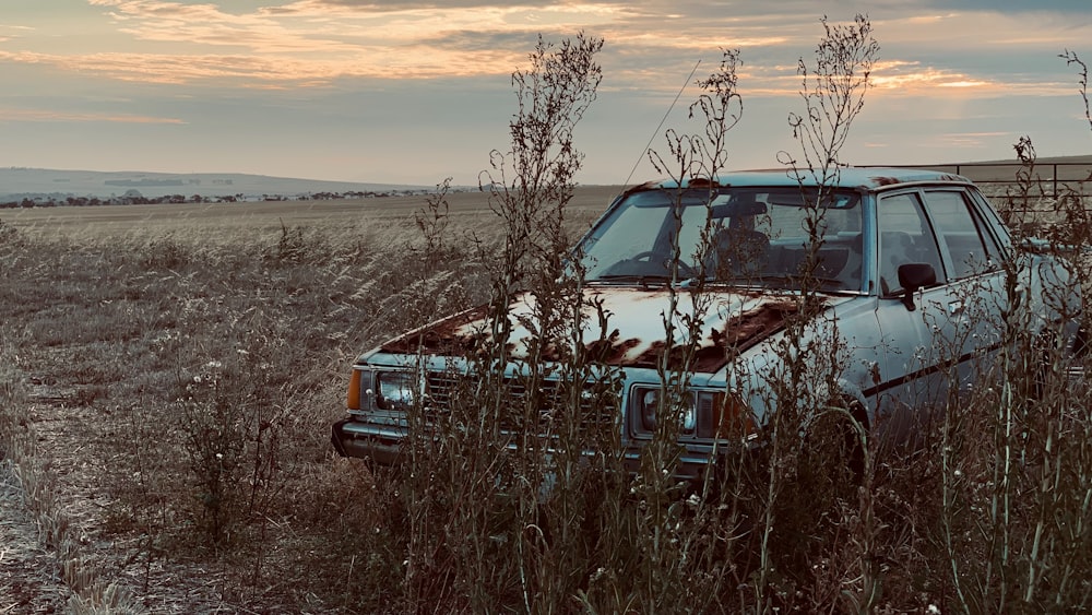 a rusted car sitting in a field of tall grass