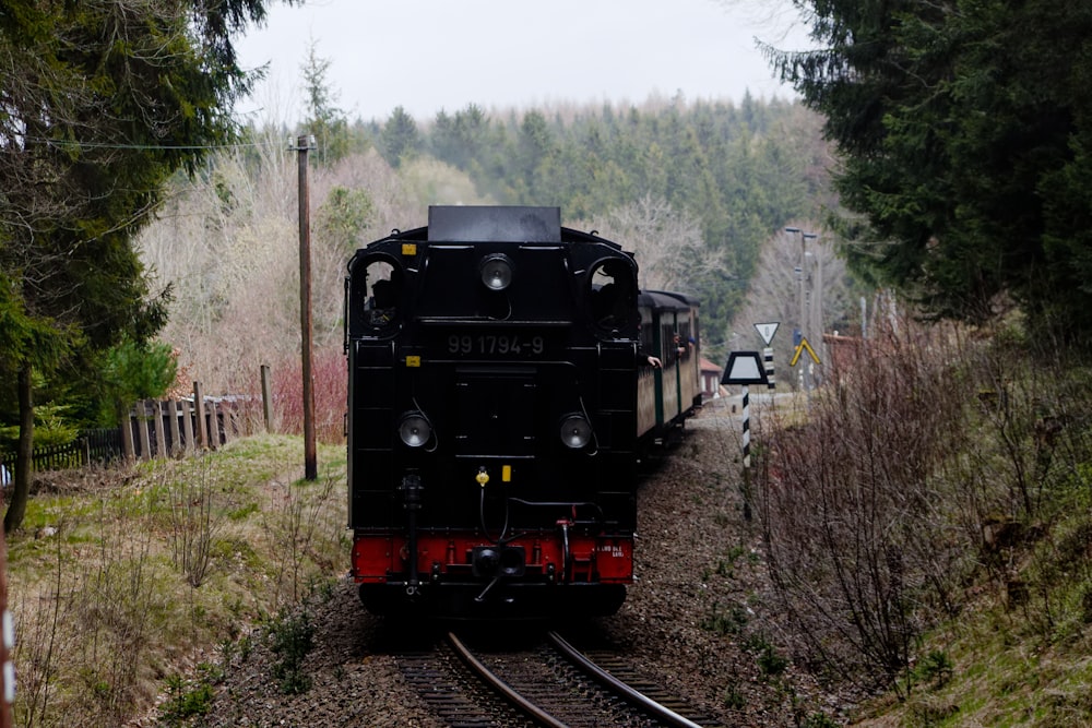 a black train traveling down train tracks next to a forest