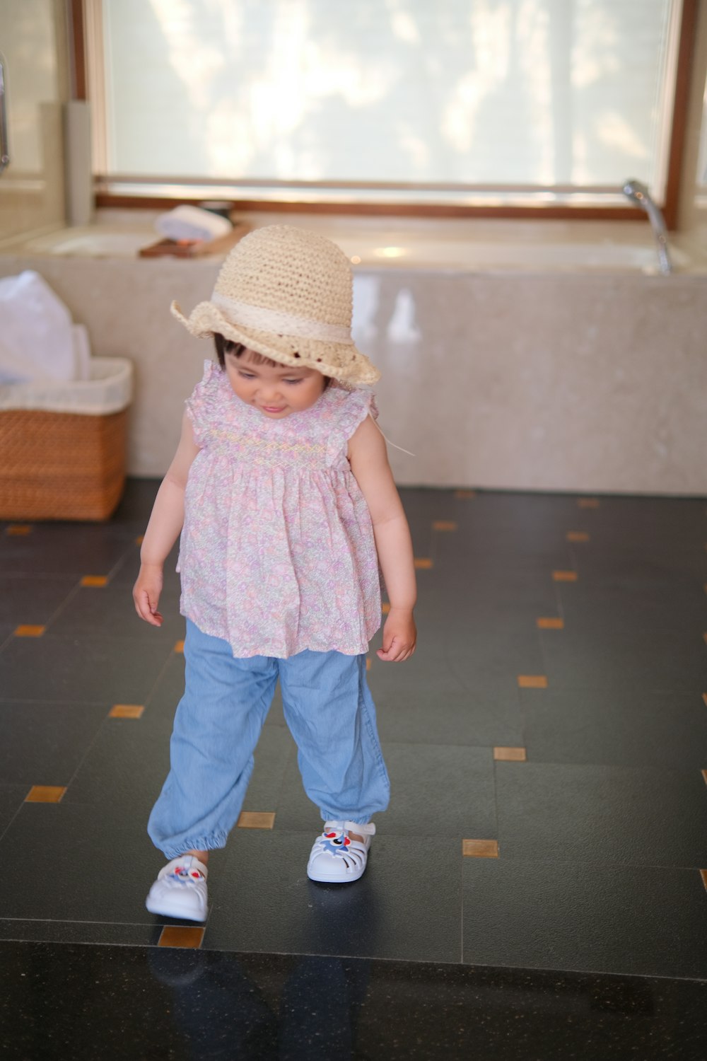 a little girl wearing a straw hat standing in front of a window