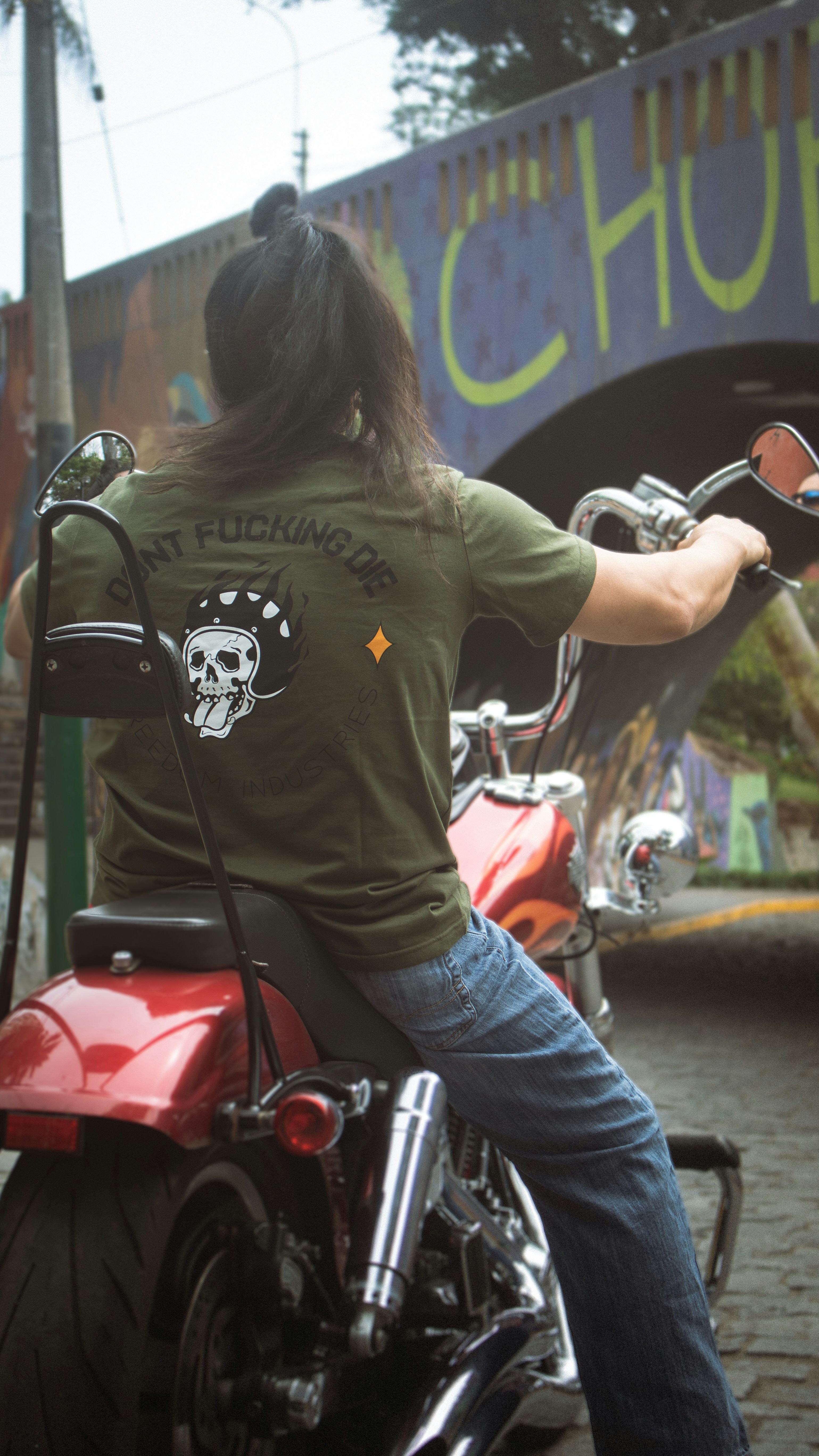 Fotomural a woman sitting on a motorcycle in front of a bridge