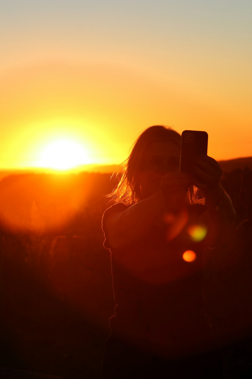 a woman taking a picture of a sunset with her cell phone