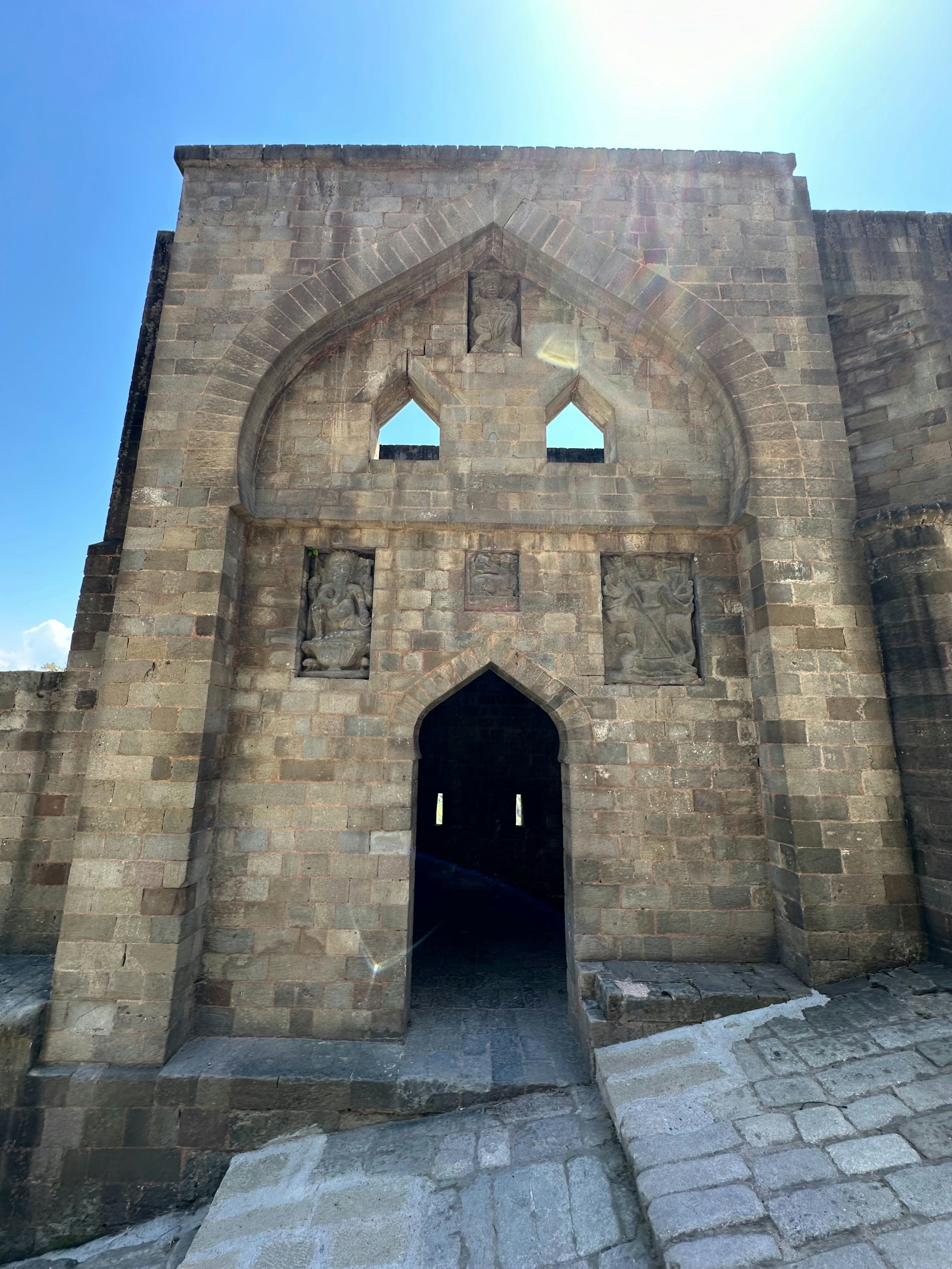 Stone temple entrance with ornate carvings, warm morning light, deep shadow archways