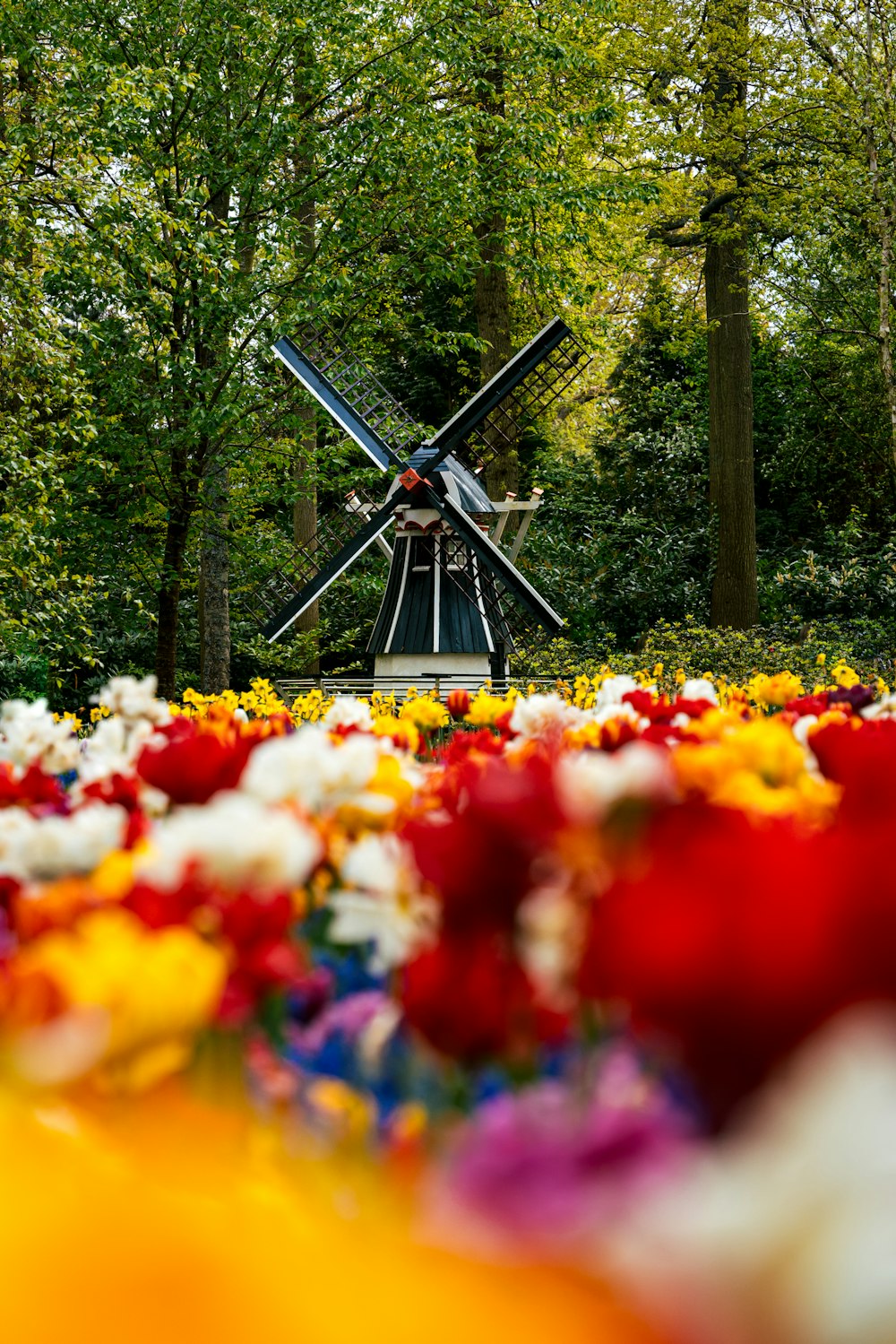 a windmill in a field of flowers with trees in the background