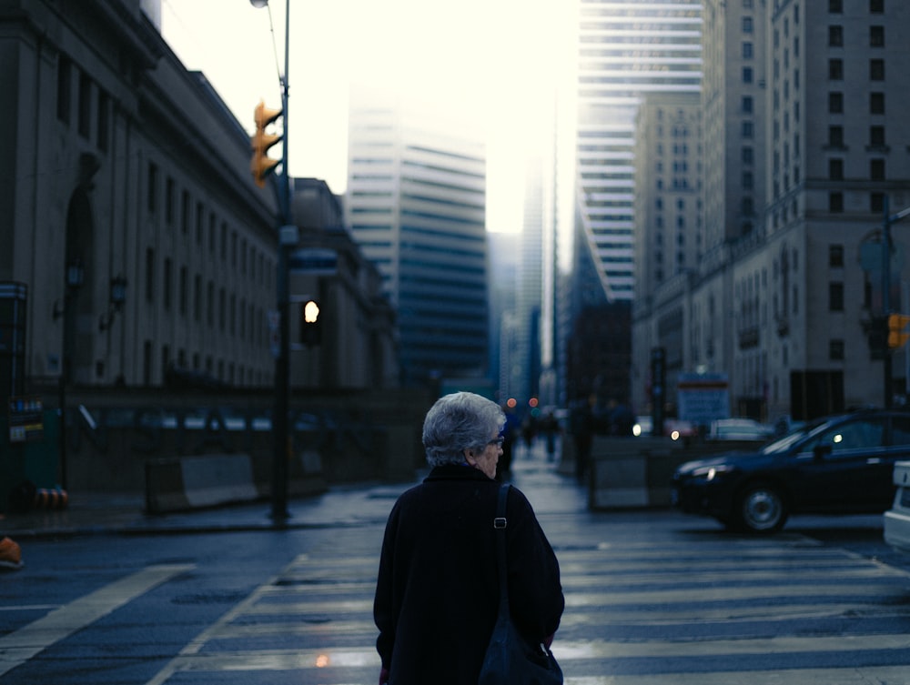 a woman walking across a cross walk in the middle of a city