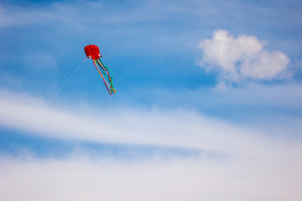 a red kite flying through a blue cloudy sky