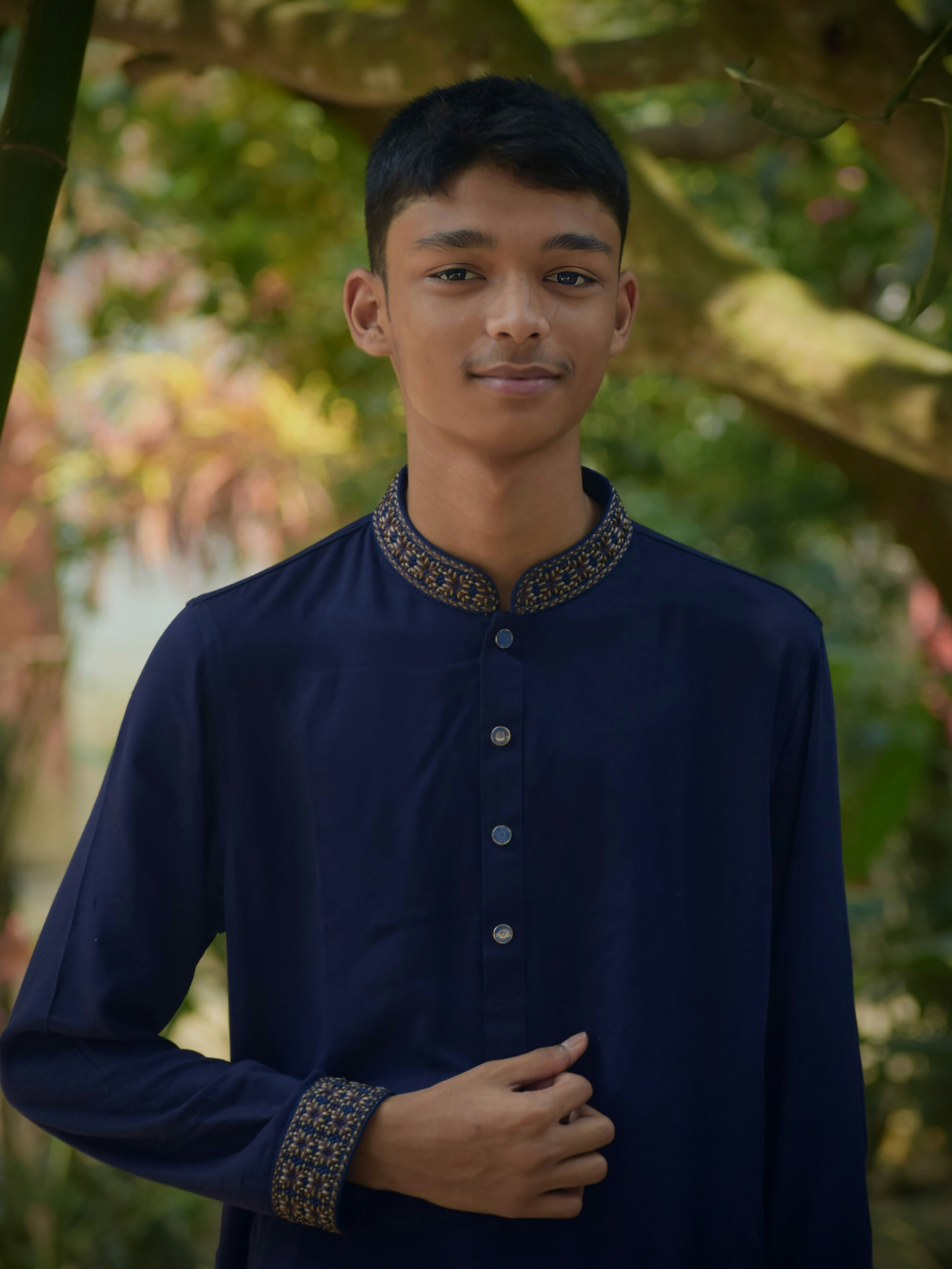 A young man standing under a tree wearing a blue shirt