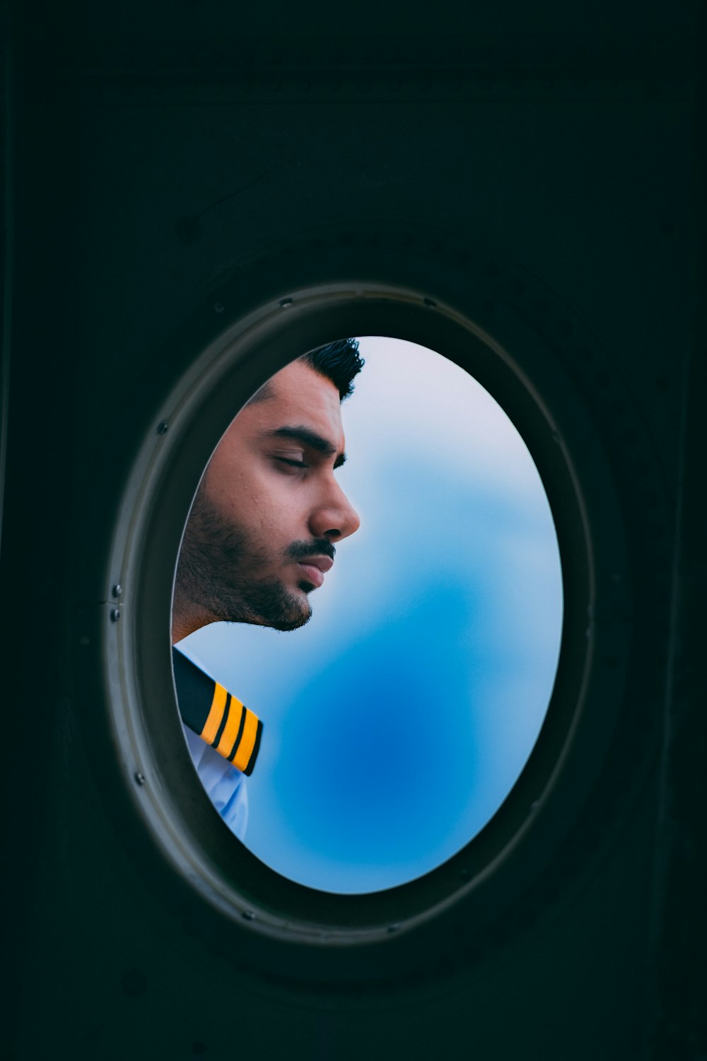 a man in a sailor's uniform looking out of a porthole window