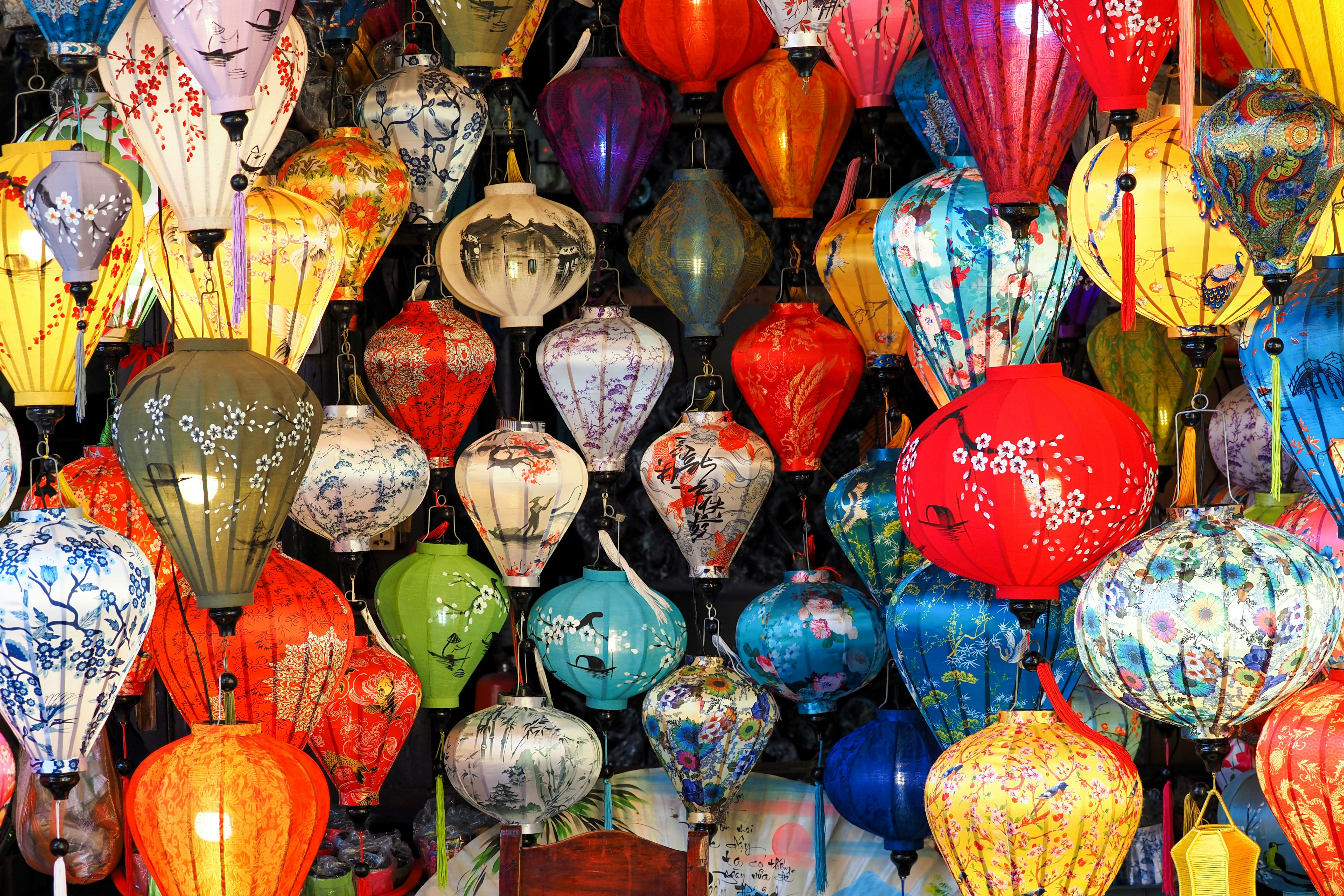 a bunch of colorful lanterns hanging from a ceiling, Hoi An Photography | Many types of lanterns with different colors and designs are seen at a shop in the ancient town of Hoi An, Vietnam.