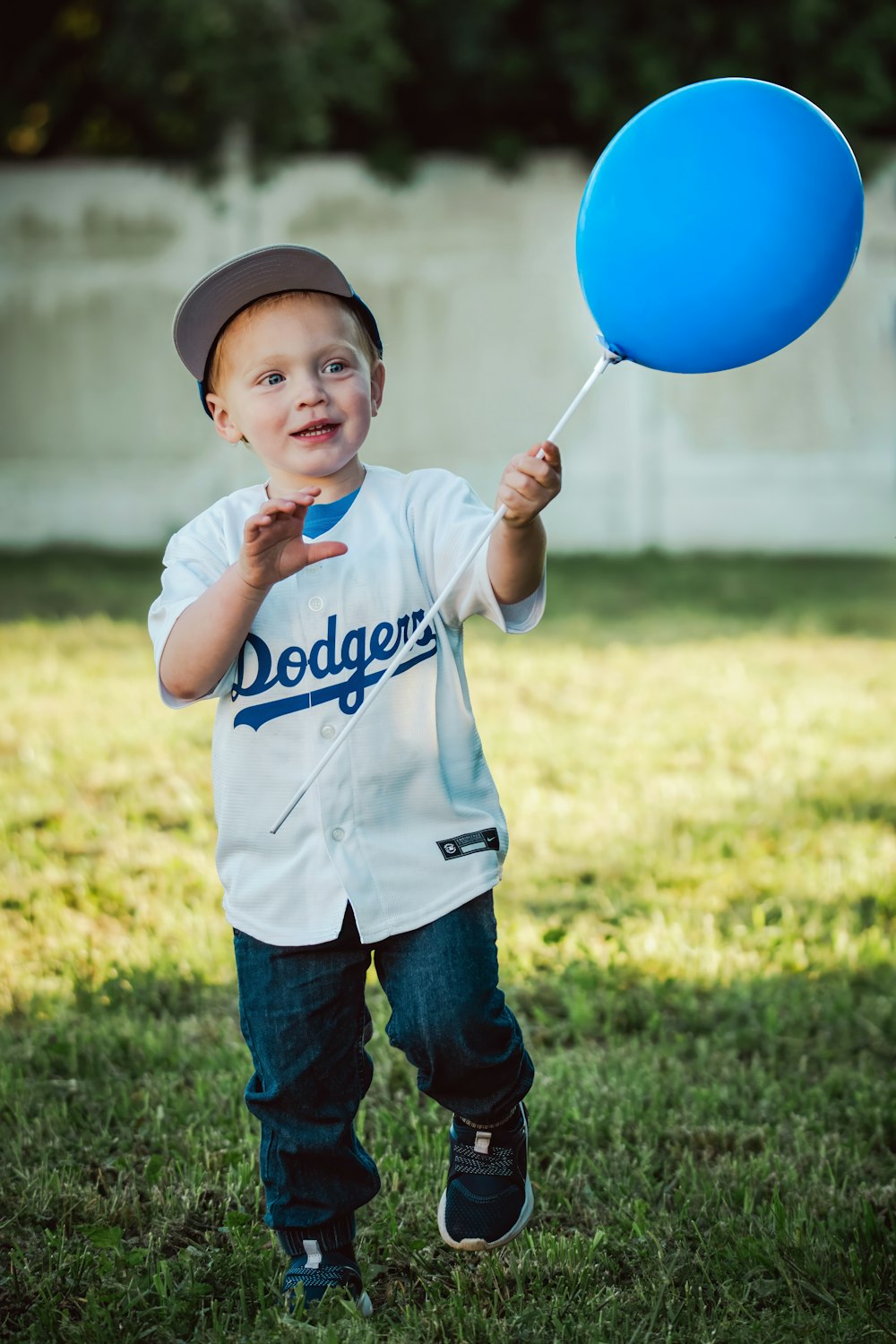 a young boy in a baseball uniform holding a blue balloon