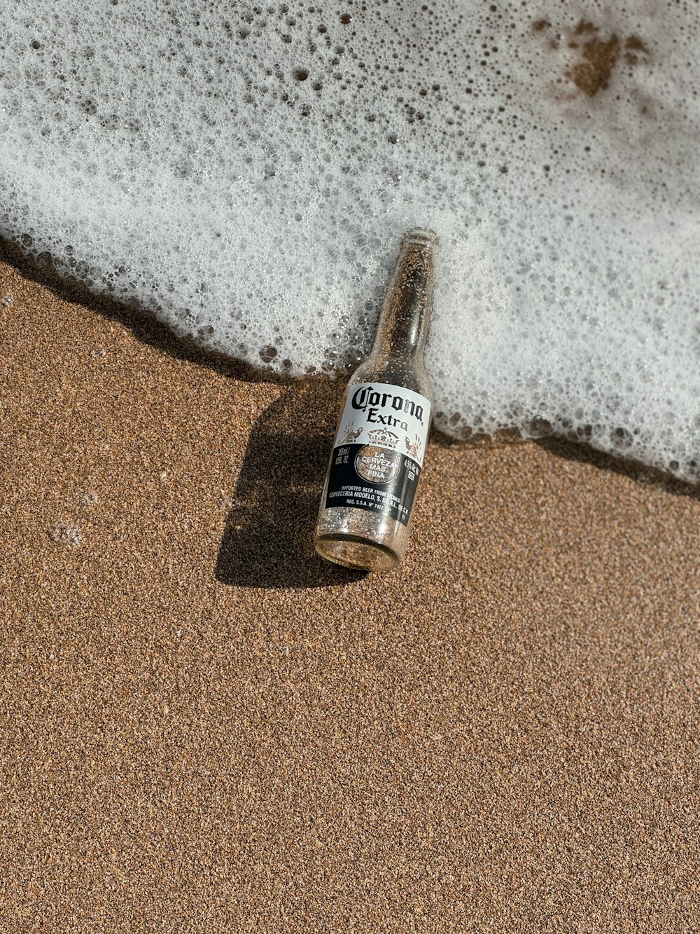 a bottle of beer sitting on top of a sandy beach