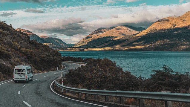 a van driving down a road next to a lake