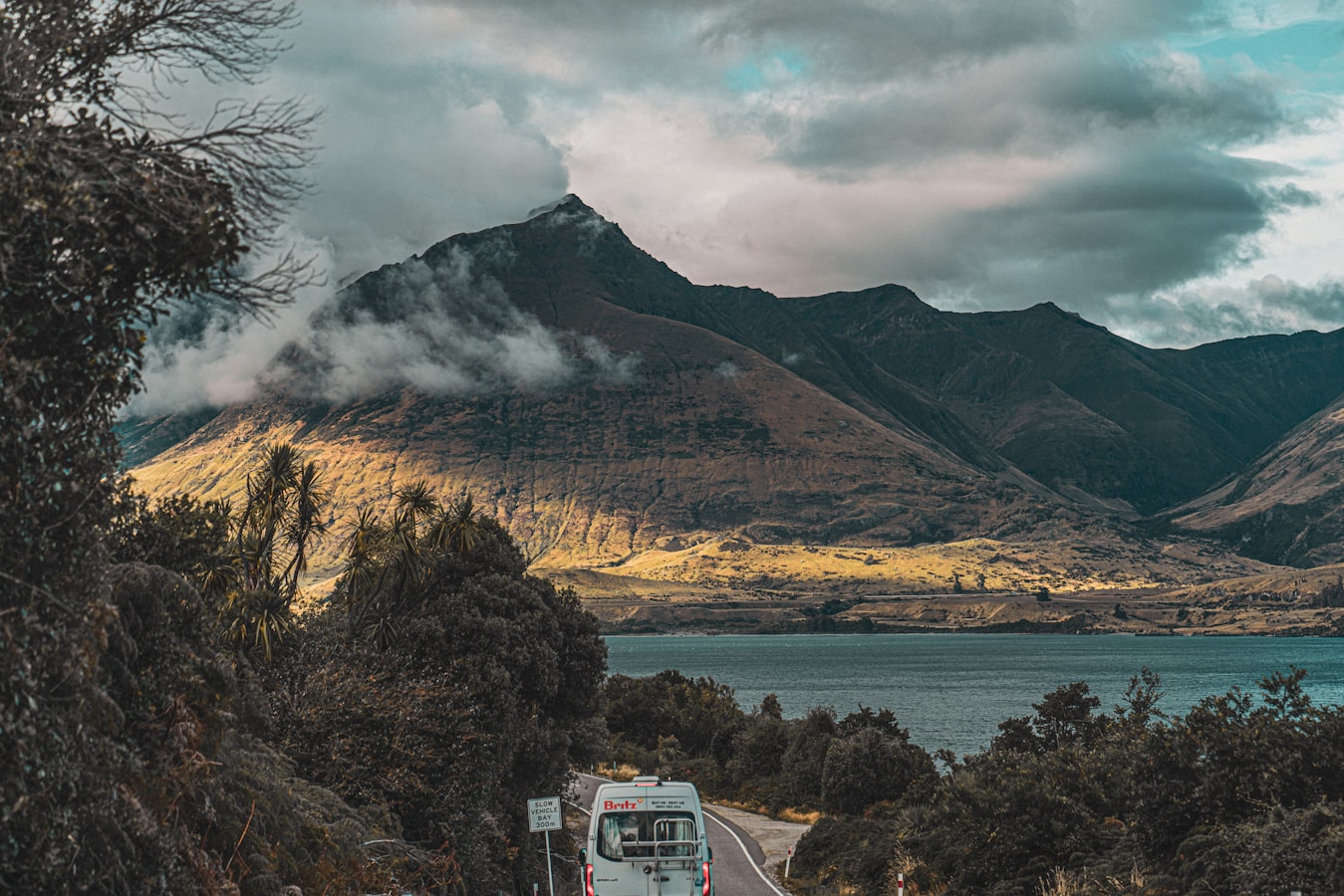 a bus driving down a road next to a mountain
