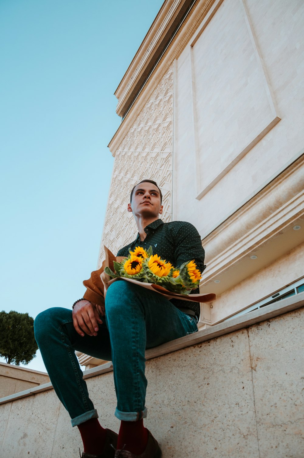 a man sitting on a ledge holding a bouquet of sunflowers