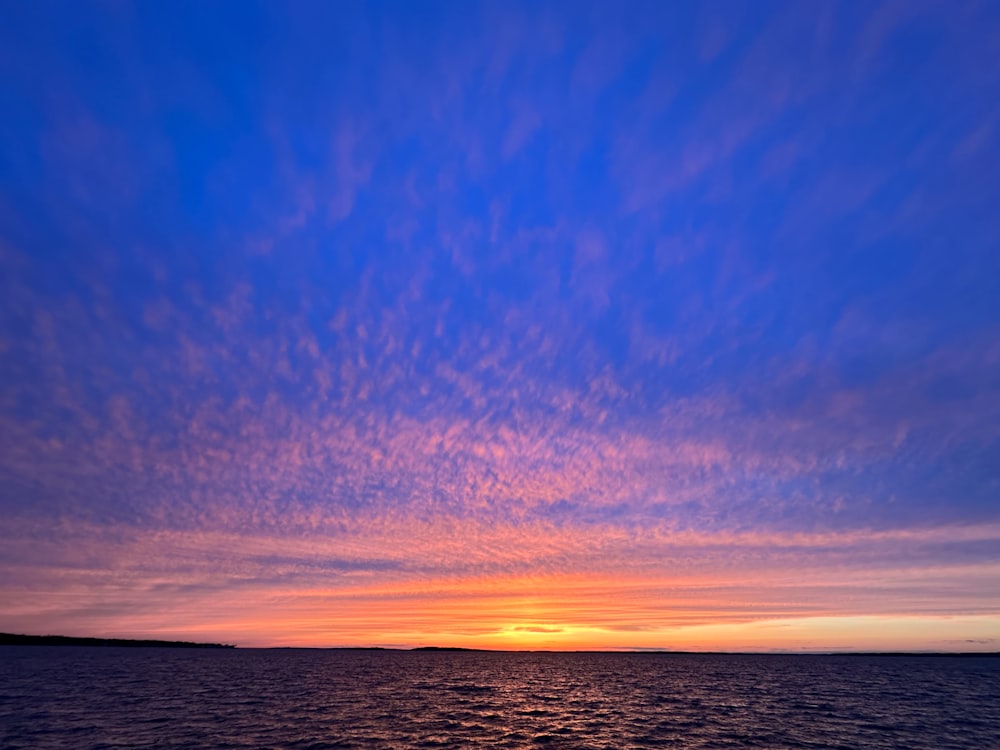 un coucher de soleil sur un plan d’eau avec des nuages dans le ciel