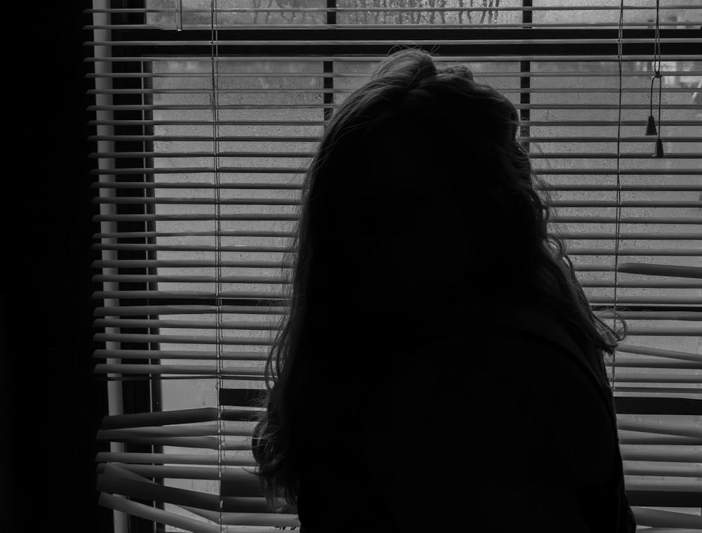 a woman standing in front of a window with blinds