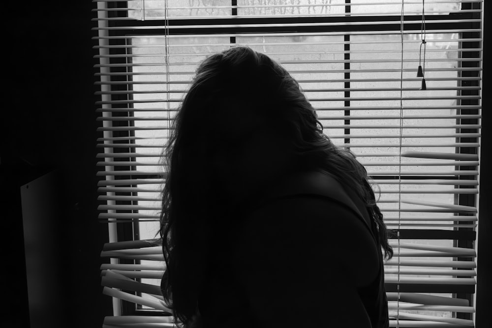 a woman standing in front of a window with blinds