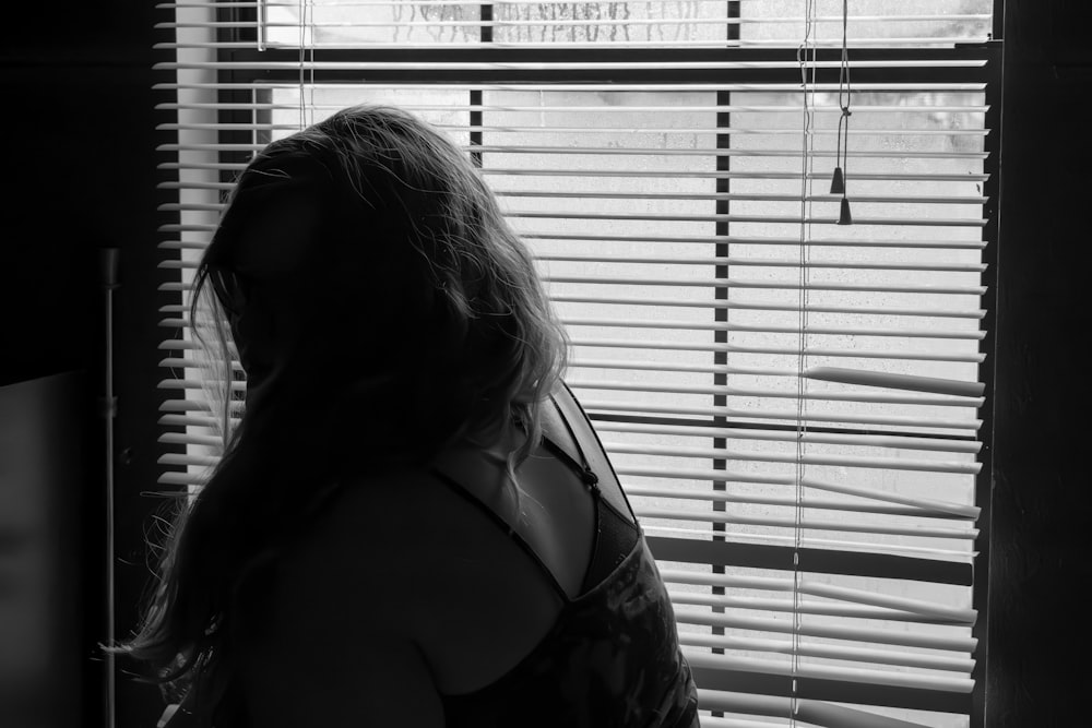 a woman standing in front of a window with blinds