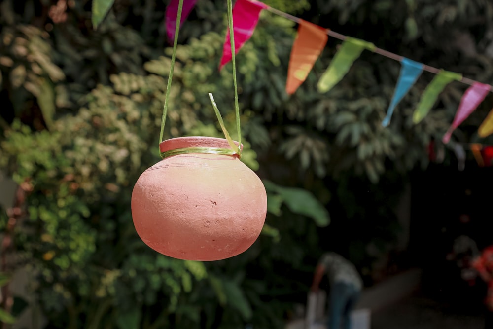 a pink vase hanging from a string in front of a forest