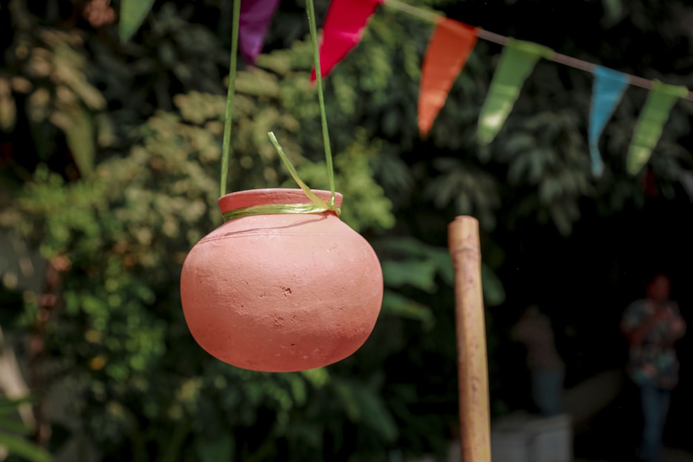 a pink vase hanging from a string with a green handle