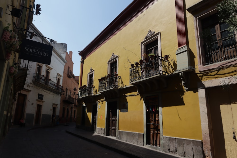 a narrow street with a yellow building with balconyes