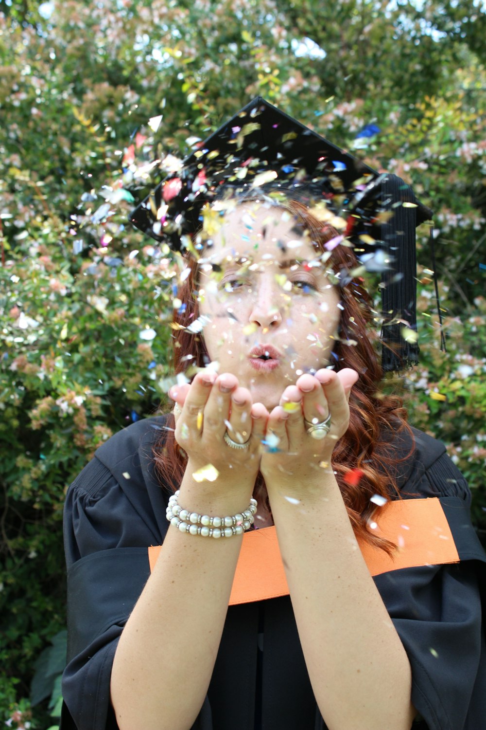 a woman in a graduation gown blowing confetti