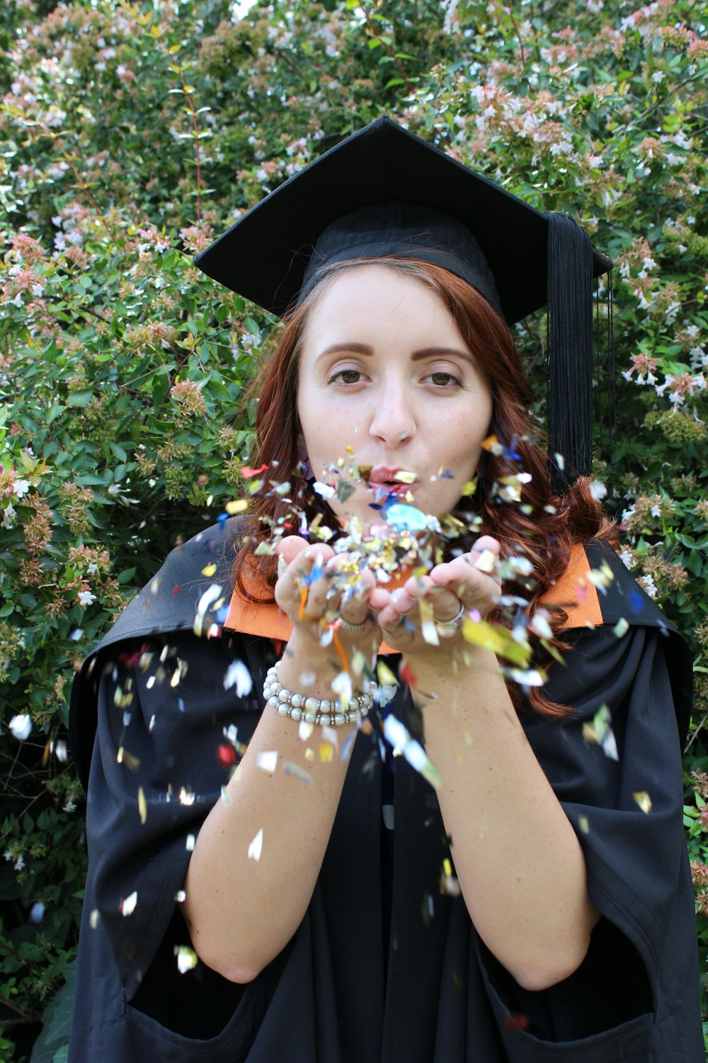 a woman in a graduation gown blowing confetti