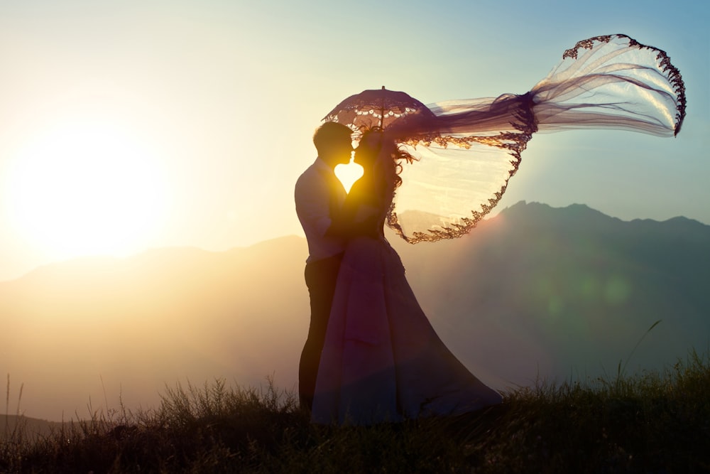 a bride and groom holding an umbrella in front of the sun
