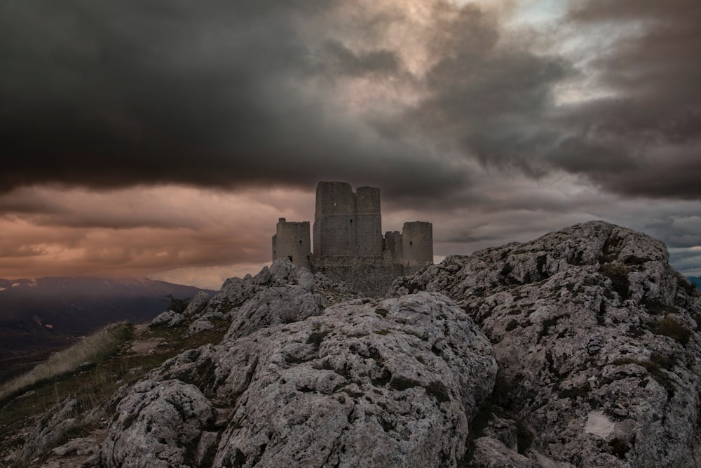 a castle sitting on top of a rocky hill under a cloudy sky