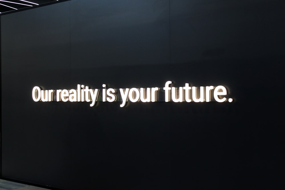 a black wall with a neon sign that says our reality is your future