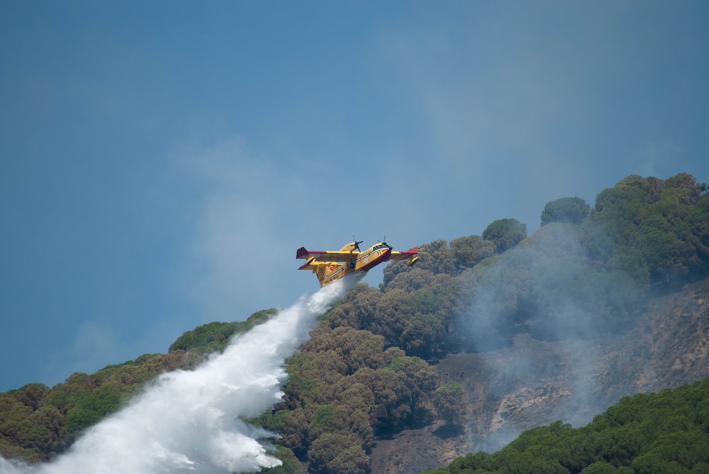 a yellow and red plane flying over a forest