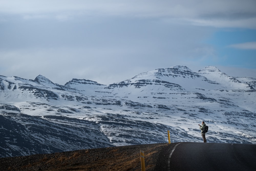 a person standing on the side of a road in front of snow covered mountains