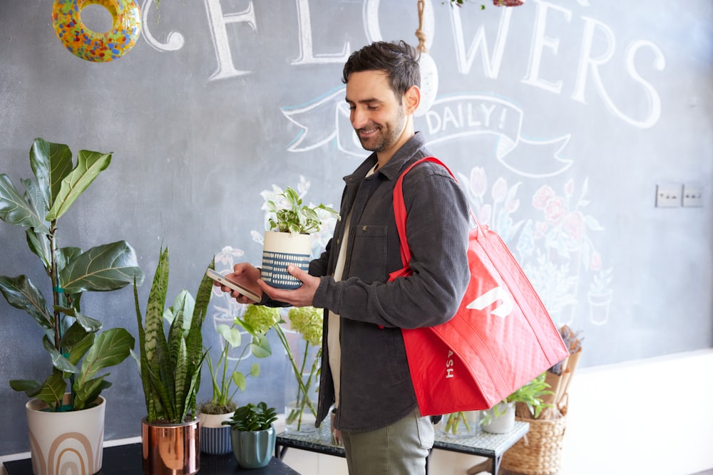 hombre curioseando una planta en la floristería con la bolsa de entrega DoorDash