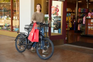 girl walking her bike by stores with DoorDash bag