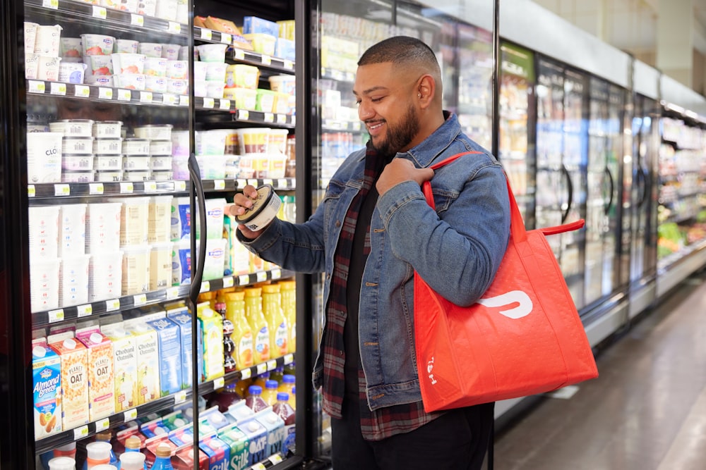 maschio che sfoglia merci refrigerate in negozio con borsa DoorDash