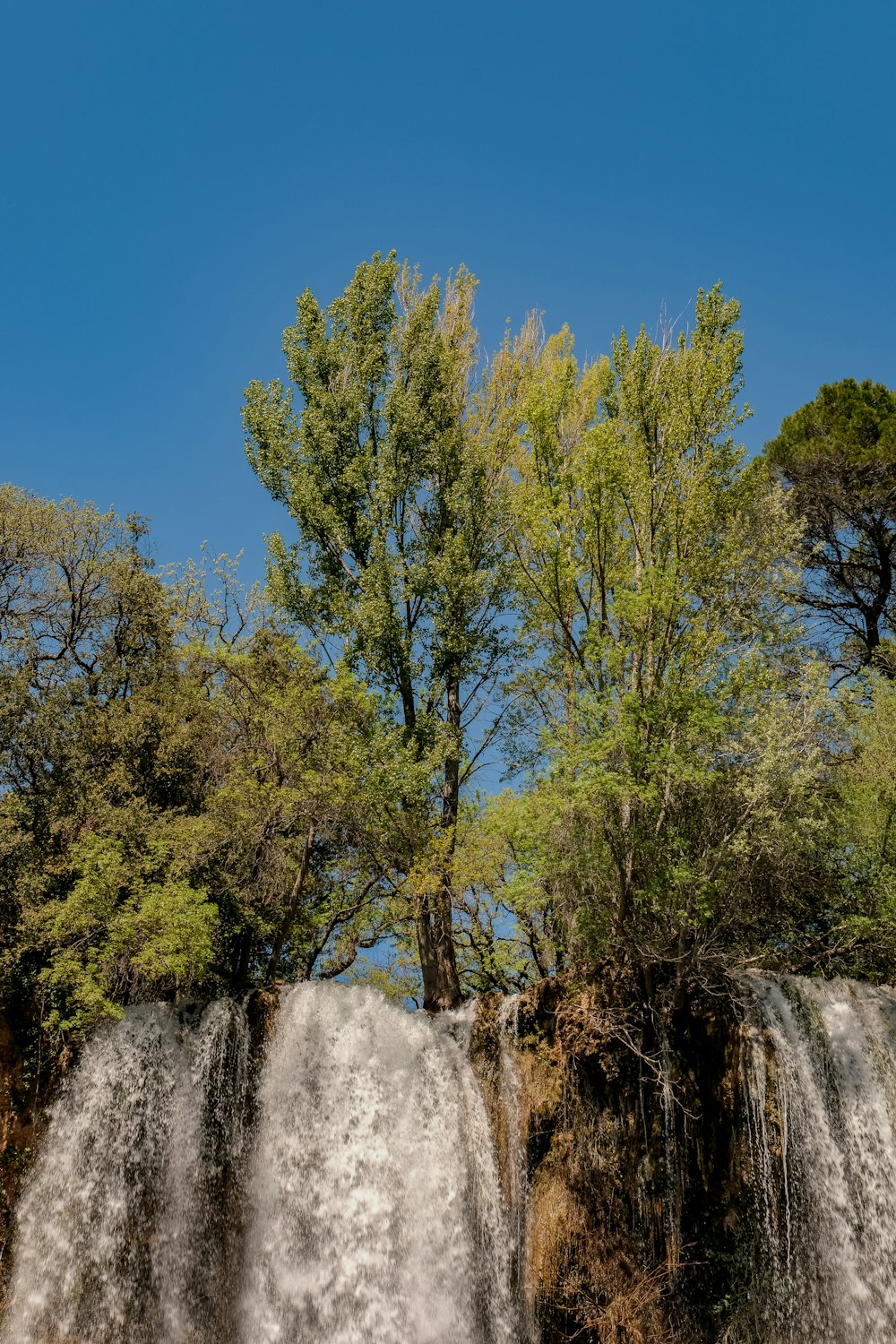 a waterfall with trees and a blue sky in the background