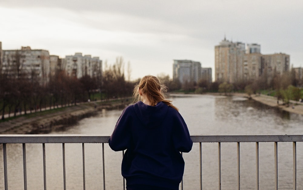 a woman standing on a bridge looking at a river