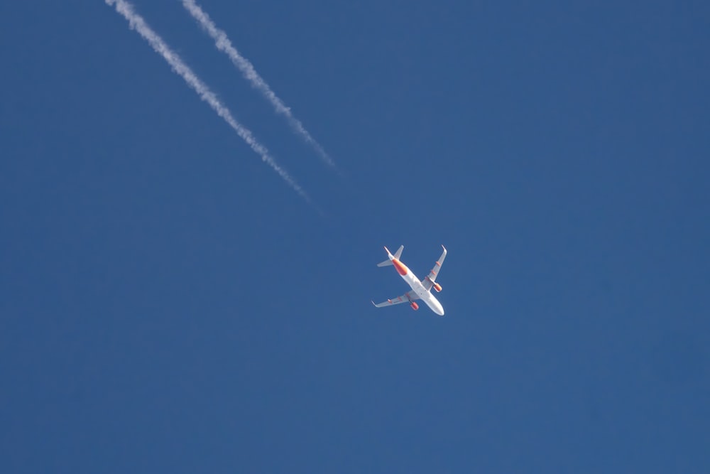 ein Flugzeug, das mit einem Kondensstreifen im Rücken am Himmel fliegt