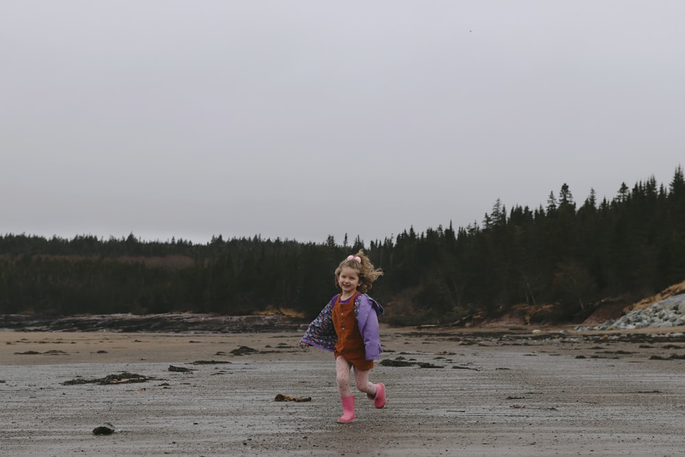 a little girl running across a sandy beach