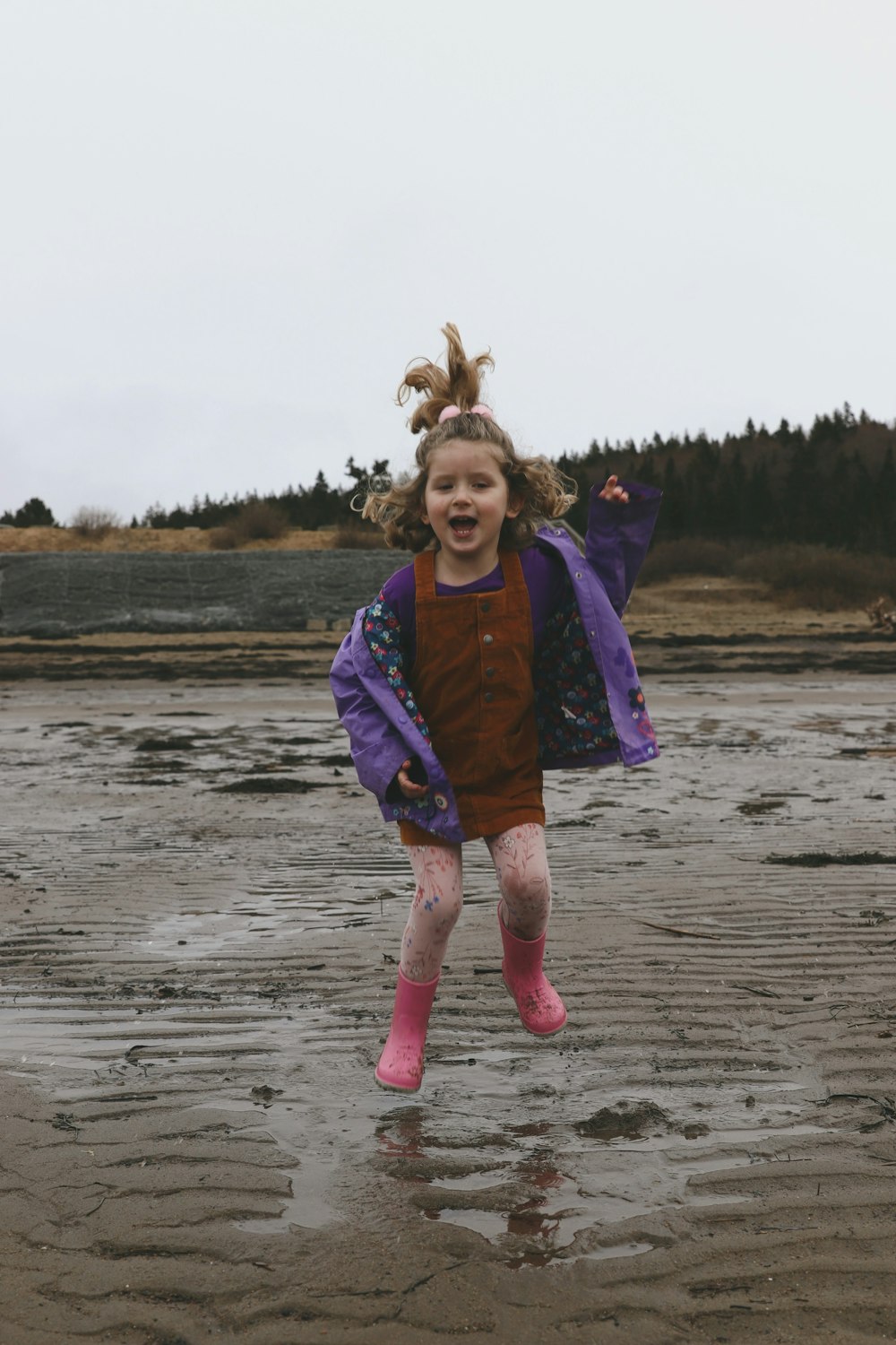 a little girl jumping in the air on a wet beach