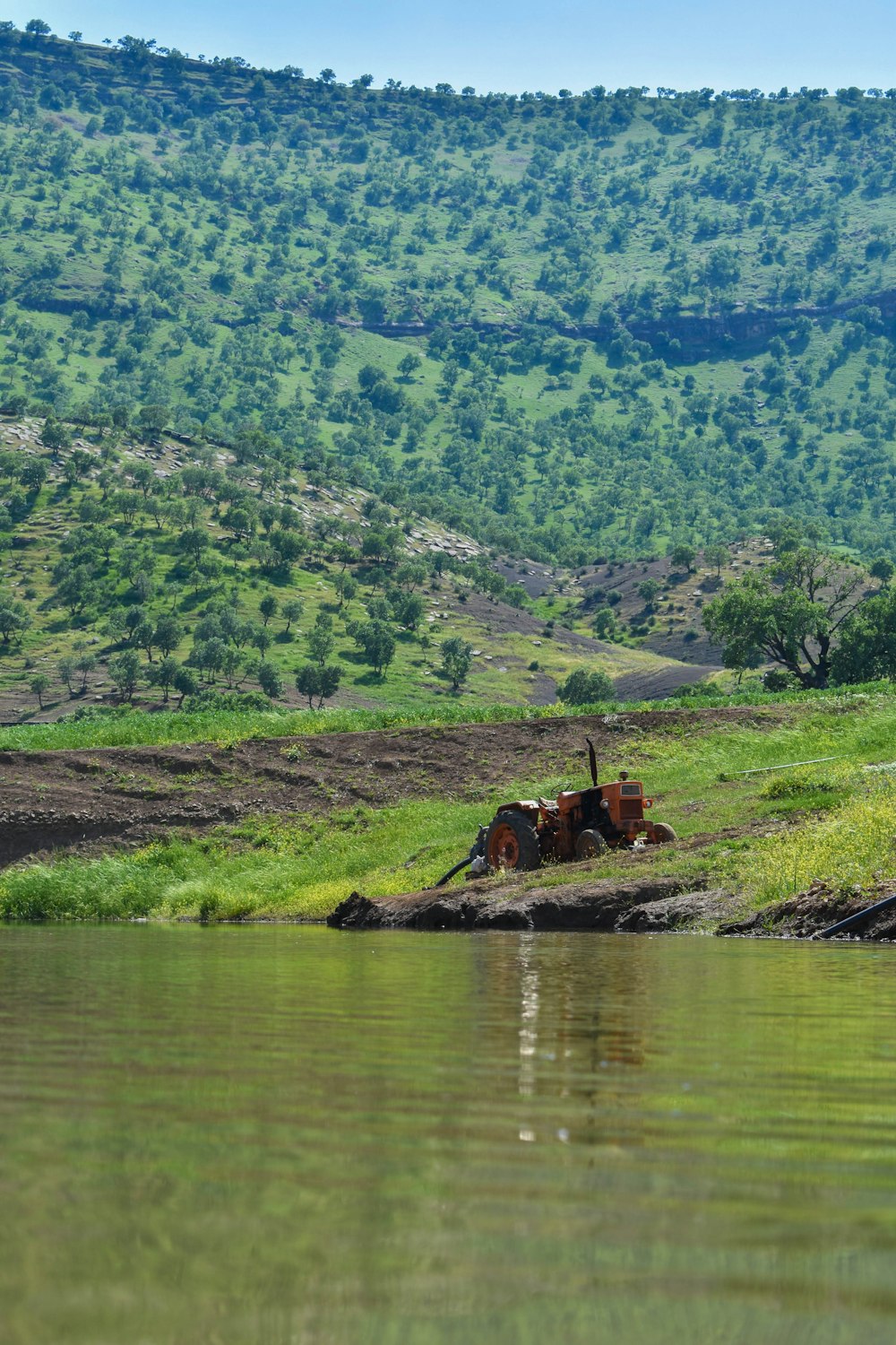 an old tractor sitting on the bank of a river