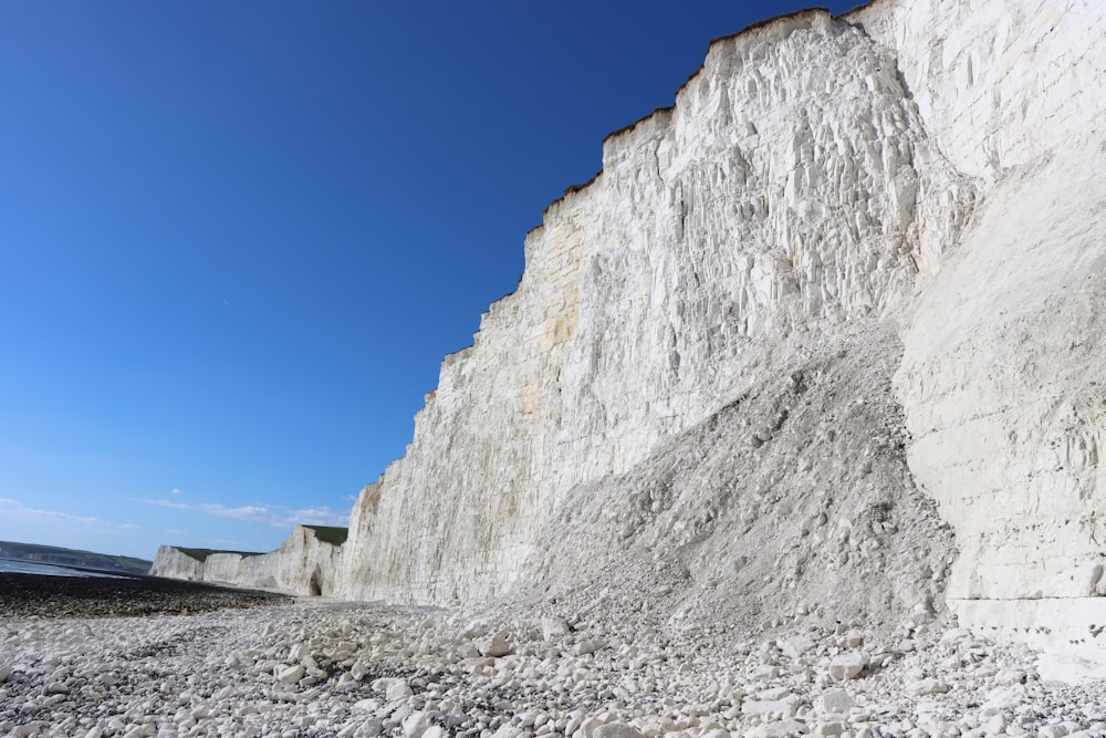 a rocky beach next to white cliffs under a blue sky